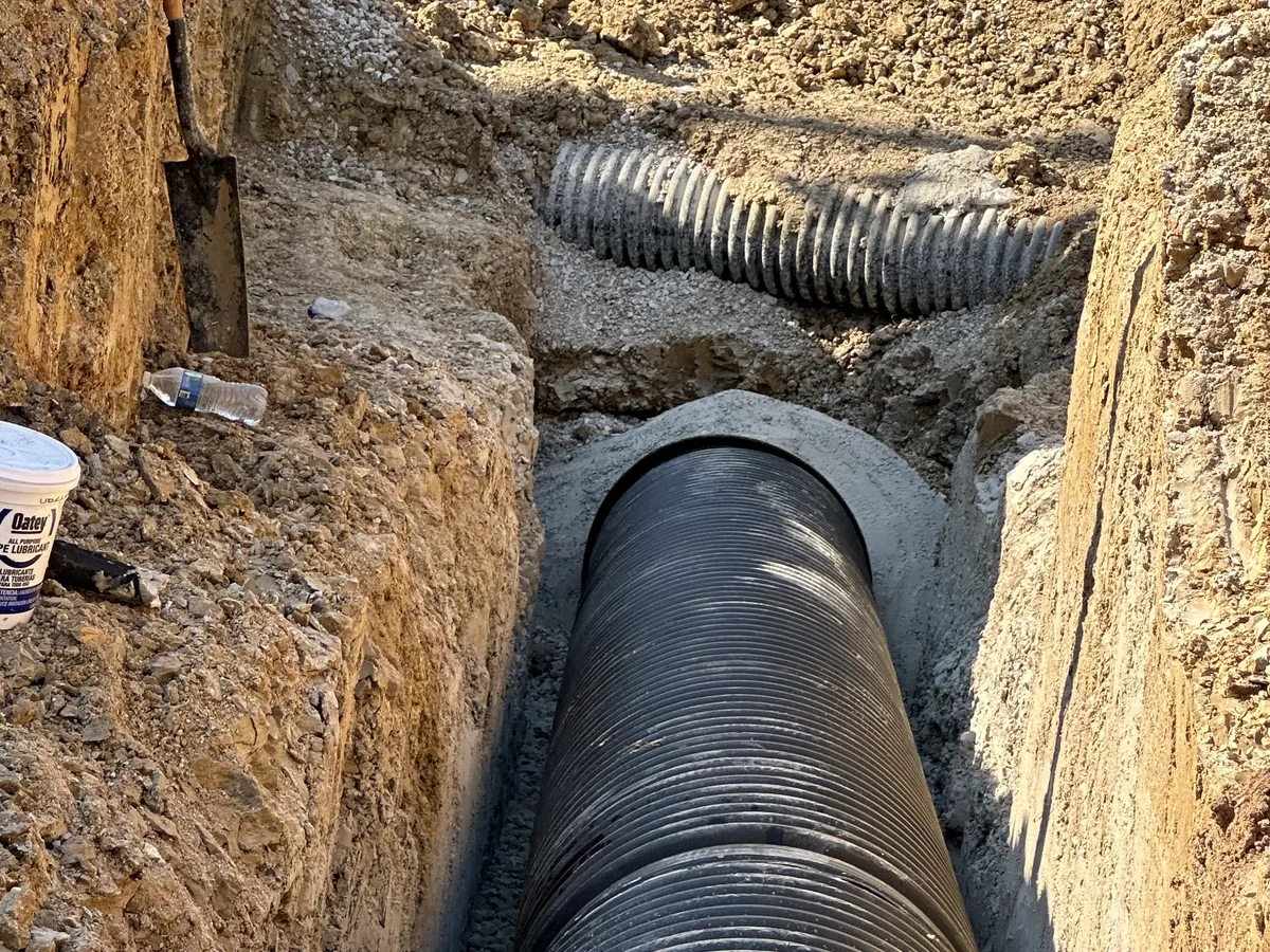 Large corrugated storm pipe running through a deep trench cut into red clay soil in Greenville, Texas